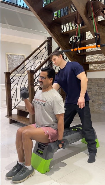 Older DeltaFit client completing a seated dumbbell exercise with a trainer